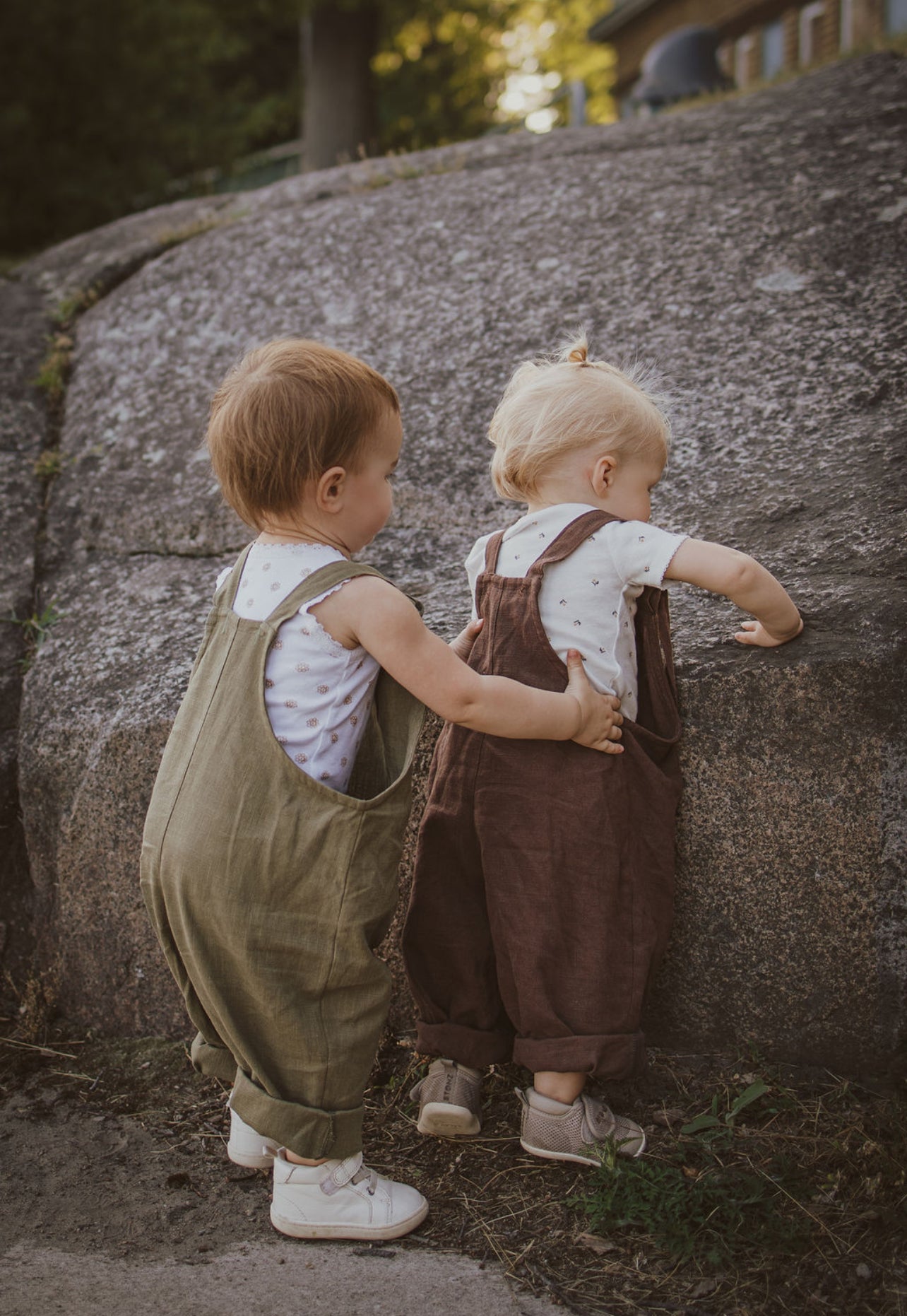 Babies playing together. Back view of linen overalls