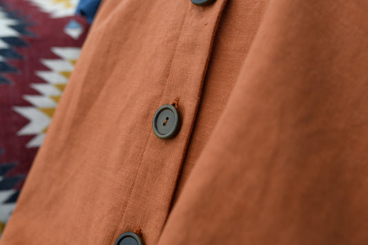 An up close image of an orange linen dress with natural buttons